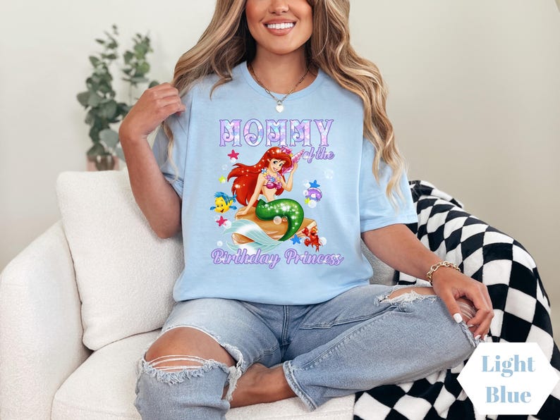 Peut inclure: T-shirt bleu clair avec un motif de sir&egrave;ne, de poissons et le texte "Mommy of the Birthday Princess". Le t-shirt est de couleur bleu clair.