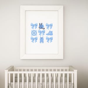 May include: A framed print with a blue and white design featuring a baby's outfit, a shoe, a bow, and a pacifier.