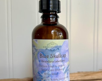 May include: A brown glass bottle with a dropper top, labeled "Blue Skullcap (Scutellaria Lateriflora)" and "Tincture Fresh in Organic Sugar-Cane Ethanol (2 fl oz/ 60 ml)". The label also includes instructions to take 2-5 ml up to 3x daily and to store in a dark place.