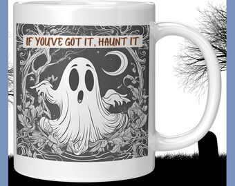 Op de afbeelding: Witte keramische mok met een spookachtig spookontwerp en de tekst "IF YOU'VE GOT IT, HAUNT IT". Het ontwerp bevat een spook, een halve maan en bladeren in zwart en wit. De mok heeft een wit handvat.
