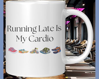 May include: White ceramic coffee mug with the text "Running Late Is My Cardio" and a row of colorful cartoon sneakers printed on the front. The mug is in focus and the background is blurry.