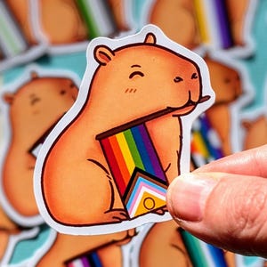 Peut inclure: Plusieurs autocollants représentant un capybara de dessin animé tenant un drapeau arc-en-ciel. Les autocollants sont de couleur marron clair et montrent le capybara dans différentes poses. Le drapeau arc-en-ciel comprend les couleurs du drapeau de la fierté LGBTQ+.