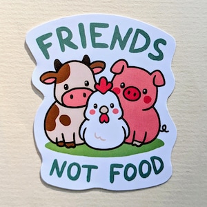 Könnte beinhalten: Ein Aufkleber mit einer Kuh, einem Schwein und einem Huhn mit dem grünen Text "FRIENDS NOT FOOD". Die Kuh ist braun und weiß, das Schwein ist rosa und das Huhn ist weiß mit einem roten Kamm. Die Tiere sind auf einem grünen Fleck.