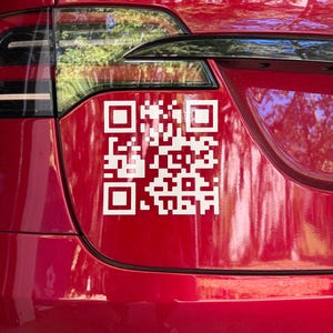 May include: A red car's rear with a white QR code sticker. The sticker is a square pattern of black and white squares. The car's taillight and a portion of the bumper are visible.