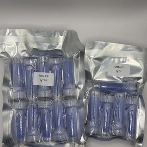 May include: Two sealed silver pouches containing multiple small, blue vials. Each pouch has a white label with the text "AHK-CU" and "1g*10" or "1g*5". The vials are cylindrical with a clear, screw-on cap. The background is plain white.