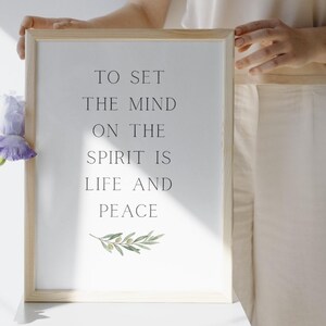 Könnte beinhalten: Ein gerahmter Druck mit dem Text "TO SET THE MIND ON THE SPIRIT IS LIFE AND PEACE" in Schwarz. Der Druck hat einen hellen Holzrahmen und eine Aquarellillustration eines Olivenzweigs unten.