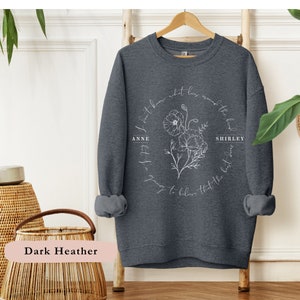 May include: Dark heather grey sweatshirt with a white floral design and the text "I don't know what lies around the bend, but I'm going to believe that the best days are yet to come." with the names "Anne" and "Shirley" on either side of the floral design.