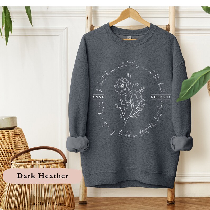 May include: Dark heather grey sweatshirt with a white floral design and the text "I don't know what lies around the bend, but I'm going to believe that the best days are yet to come." with the names "Anne" and "Shirley" on either side of the floral design.