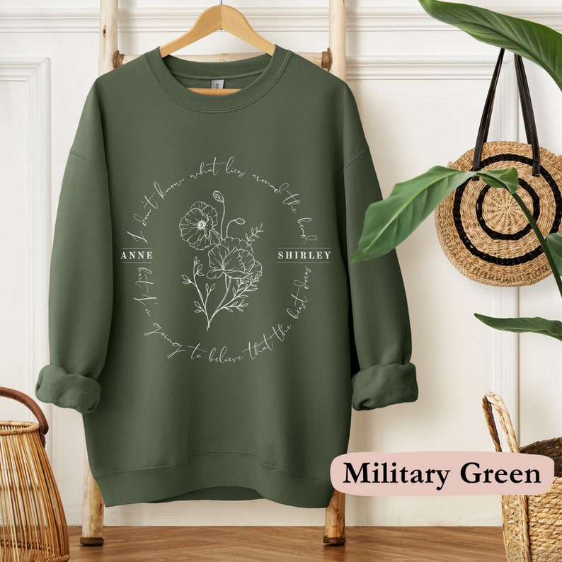 May include: A military green sweatshirt with a white floral design and the text "I don't know what lies around the bend, but I'm going to believe that the best days are yet to come."  The names "Anne" and "Shirley" are included in the text.