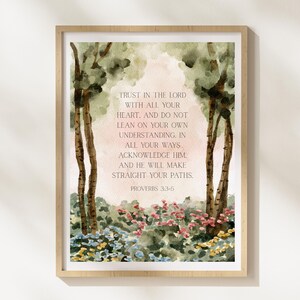 Op de afbeelding: Ingelijste aquarelprint in een licht houten frame met een serene landschap met bomen en bloemen. De tekst "TRUST IN THE LORD WITH ALL YOUR HEART..." uit Spreuken 3:3-5 is opgenomen. Het kleurenpalet omvat groen, roze en bruin.