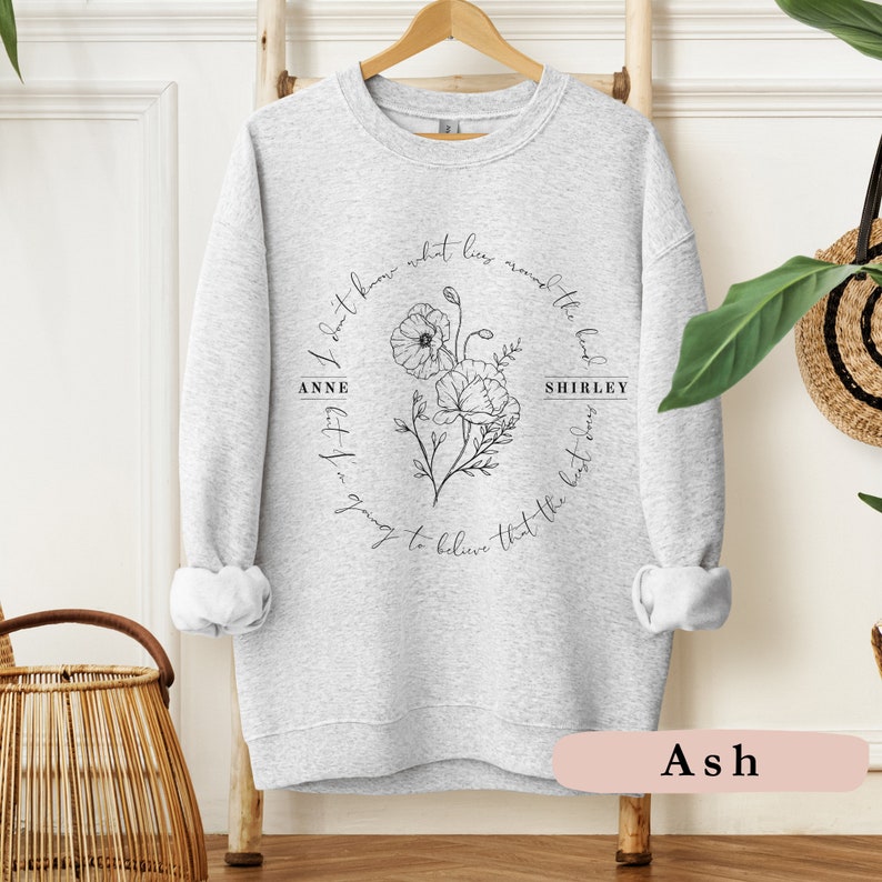 May include: Gray sweatshirt with a black floral design and the text "I don't know what lies around the bend but I'm going to believe that the best is yet to come" with the names "Anne" and "Shirley" on either side of the floral design.