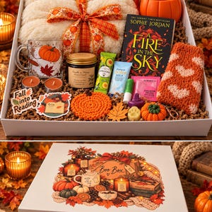 Könnte beinhalten: Eine Geschenkbox mit einer cremefarbenen, flauschigen Decke mit Kürbisband, einer orangefarbenen Kürbistasse, dem Buch A Fire in the Sky von Sophie Jordan, einem Glasbecher, einer Vanille-Honig-Kerze, Hautpflegeprodukten, flauschigen Socken und Herbstaufklebern.