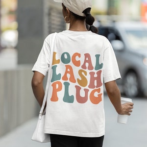 Pode incluir: Camiseta branca com o texto "LOCAL LASH PLUG" em letras retrô coloridas.