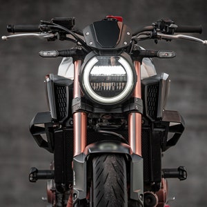 May include: A white and copper motorcycle with a black headlight and black windscreen. The motorcycle is on a motorcycle stand.