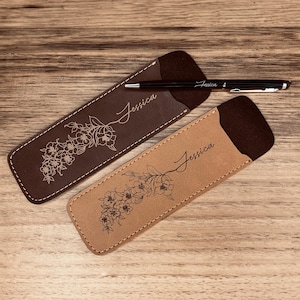 Puede incluir: Dos portaplumas de cuero marrón con un diseño floral y el nombre "Jessica" grabado en cada uno. Un portaplumas es marrón y el otro es beige.