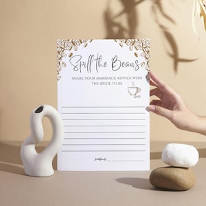 Può includere: Un taccuino bianco con il testo "Spill the Beans" e righe per scrivere consigli. Il taccuino è decorato con illustrazioni di chicchi di caffè. Un vaso di ceramica bianca e pietre impilate sono anche nell'immagine.