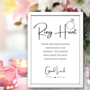 May include: White sign with black text that reads "Ring Hunt" and "There are rings hidden throughout the shower. The person who finds the most rings wins a prize!"  The sign also has a small drawing of a ring with a diamond and the words "Good Luck" written in cursive.