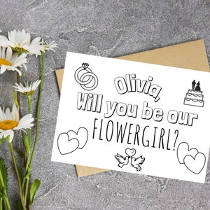 May include: A printable card with the text "Olivia, will you be our flower girl?"  The card features a wedding ring, a wedding cake, and two doves with a heart.