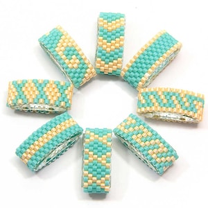 Op de afbeelding: Acht kralenringen die in een cirkelvormige opstelling zijn geplaatst. De ringen zijn gemaakt van turquoise blauwe en crèmekleurige kralen. De ringen zijn in een cirkel geplaatst met de crèmekleurige kralen naar buiten gericht.