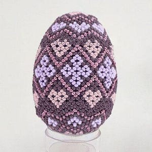 May include: A purple and pink beaded Easter egg with a geometric pattern.