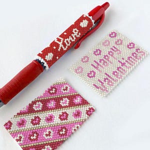 Op de afbeelding: Drie kralenstukken met een Valentijnsdagthema. Een stuk is een pen met een rode cilinder en een witte kralenkap die "Love" zegt. De andere twee stukken zijn plat en rechthoekig met roze, witte en rode kralen. Een stuk zegt "Happy Valentines".