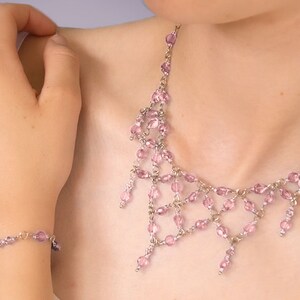 Puede incluir: Un delicado conjunto de collar y pulsera de cuentas rosas. La joyería presenta pequeñas cuentas rosas redondas ensartadas con metal plateado. El collar tiene un diseño en cascada y la pulsera es una simple hebra.