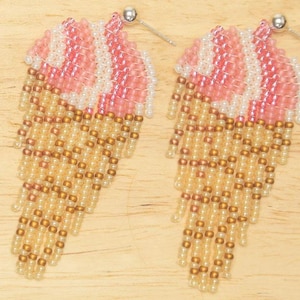 May include: A pair of pink and beige beaded earrings shaped like ice cream cones. The earrings are made with small beads and have a dangling design.