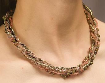 May include: A multi-strand necklace made of small beads in shades of brown, pink, and gold. The necklace is woven in a braided pattern and has a delicate, feminine look.