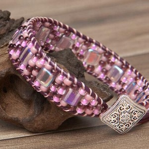 May include: A purple and pink beaded bracelet with a silver clasp. The bracelet is made with small square beads and round beads.