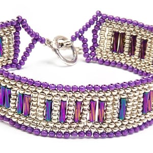 Può includere: Un braccialetto di perline viola e argento con una chiusura argentata. Il braccialetto presenta un motivo geometrico con perline rettangolari iridescenti.