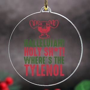 May include: Clear, round Christmas ornament with a red and green graphic and text. The graphic is of a moose head in a cocktail glass. The text reads "Hallelujah! Holy Sh*t! Where's the Tylenol".
