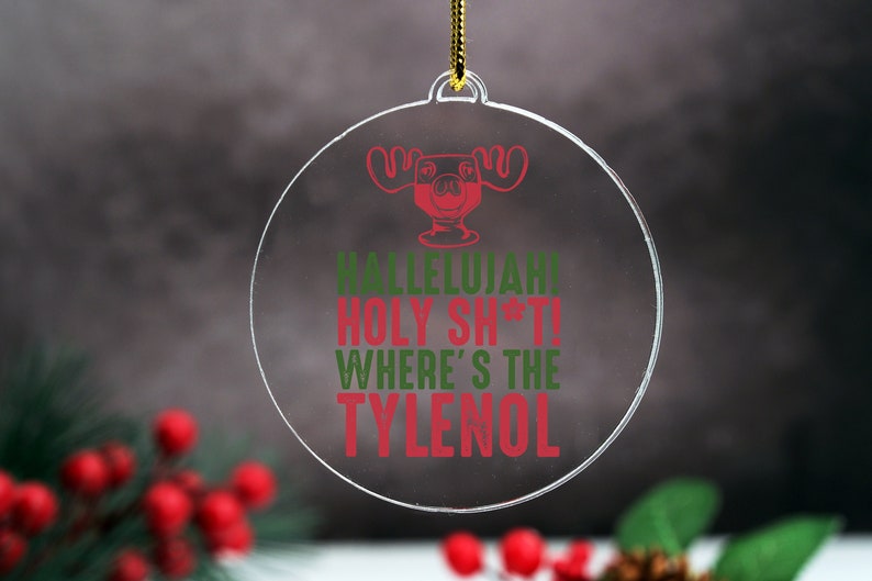 May include: Clear, round Christmas ornament with a red and green graphic and text. The graphic is of a moose head in a cocktail glass. The text reads "Hallelujah! Holy Sh*t! Where's the Tylenol".