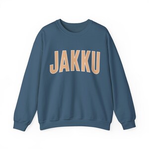 Puede incluir: Una sudadera azul oscuro con la palabra "JAKKU" impresa en color marrón claro en la parte delantera.