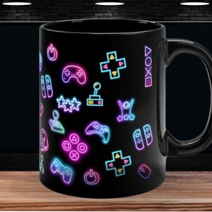 May include: Black ceramic coffee mug with a neon-colored design of video game controllers, joysticks, and other gaming symbols.