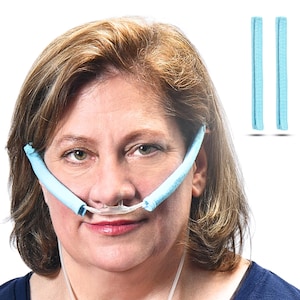 May include: A woman wearing a light blue nasal cannula with soft, padded ear loops. Two additional light blue ear loop pads are shown in the upper right corner. The woman is wearing a dark blue shirt.