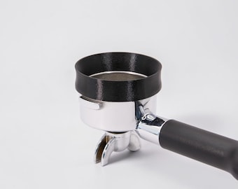 Puede incluir: Un portafiltro de espresso cromado con un mango de plástico negro y un embudo dosificador negro fijado en la parte superior de la cesta metálica. El portafiltro tiene un diseño de doble boquilla en la base y un acabado metálico pulido.