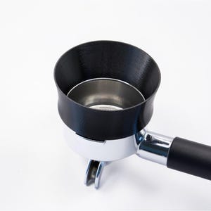 Puede incluir: Un embudo negro para portafiltro de café se encuentra sobre un portafiltro de acero inoxidable. El embudo es de plástico negro y tiene una abertura ancha y acampanada. El mango es negro y el portafiltro es cromado.