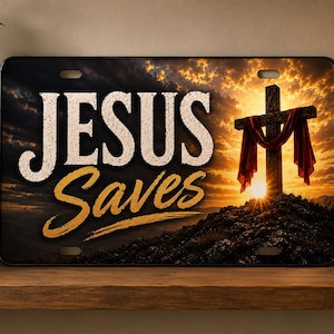 Op de afbeelding: Een rechthoekige metalen kentekenplaat met de tekst JESUS SAVES in witte en gouden letters. De achtergrond toont een zonsondergang met een donker houten kruis gedrapeerd met rode stof op een heuvel tegen een bewolkte lucht.