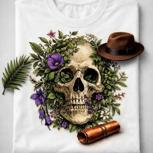 a white t-shirt with a skull design surrounded by purple flowers and green leaves, along with a brown hat and a rolled-up piece of paper.