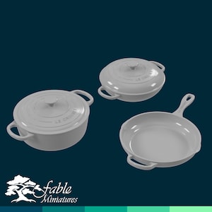 Puede incluir: Tres piezas de utensilios de cocina de hierro fundido gris: una olla con tapa, una sartén y una cacerola. Los utensilios de cocina están hechos por Le Creuset.