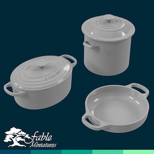 May include: Three miniature grey Le Creuset cookware items are shown against a dark teal background. The set includes a covered pot, an oval covered casserole, and a round dish. The logo "fable miniatures" is in the lower left corner.