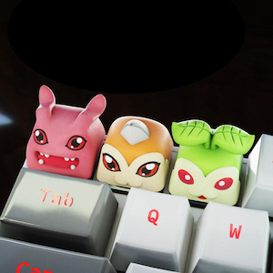 Peut inclure: Trois touches de clavier colorées avec des personnages de dessins animés. Les touches sont roses, oranges et vertes, chacune avec des traits de visage et des motifs uniques. Les touches "Tab", "Q" et "W" sont visibles.