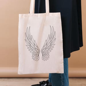Mockup image showing one of the Angel wings designs included on a canvas tote black. Black line illustration.