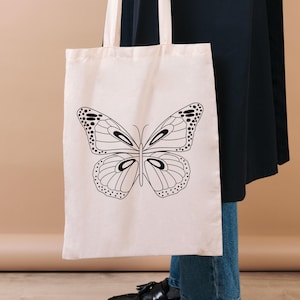 Mockup image showing one of the butterfly designs on a canvas tote black. Black line illustration.