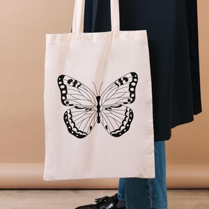 Mockup image showing one of the butterfly stamp designs on a canvas tote black. Black line illustration.