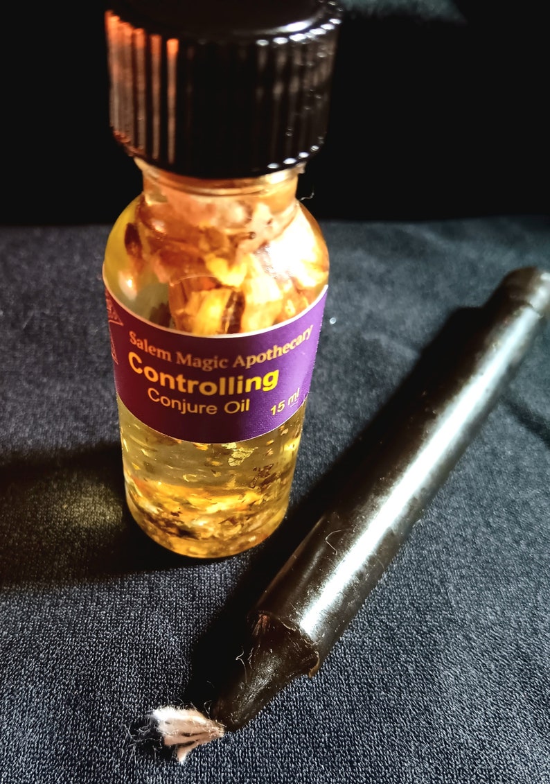 Pode incluir: Uma pequena garrafa de vidro com tampa preta cheia de um l&iacute;quido amarelo e flocos dourados. A garrafa tem um r&oacute;tulo roxo que diz "Salem Magic Apothecary Controlling Conjure Oil 15 ml".