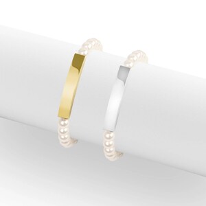 May include: Two bracelets with a pearl bead strand. One bracelet has a gold-colored rectangular bar, and the other has a silver-colored rectangular bar. The bracelets are displayed on a white surface.