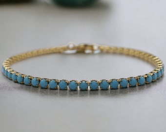 May include: A delicate gold bracelet featuring small, round, light blue gemstones set closely together. The bracelet has a simple clasp and a thin, elegant design, perfect for everyday wear.