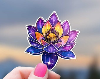 May include: A purple and yellow galaxy lotus flower sticker with glitter accents. The sticker is held in a hand against a blurred background of a sunset.