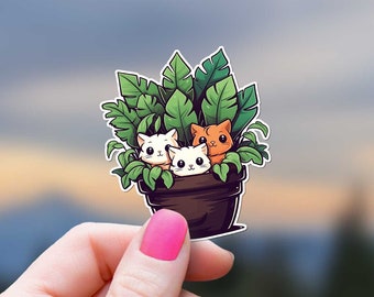 May include: A sticker of three cartoon cats peeking out of a potted plant. The cats are white with pink noses and orange eyes. The plant is green with brown leaves. The pot is brown with a white rim.